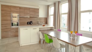 A modern kitchen with wooden cabinets, a built-in oven, and a dining area with a table and chairs. - Place2stay in Ghent (Ghent)