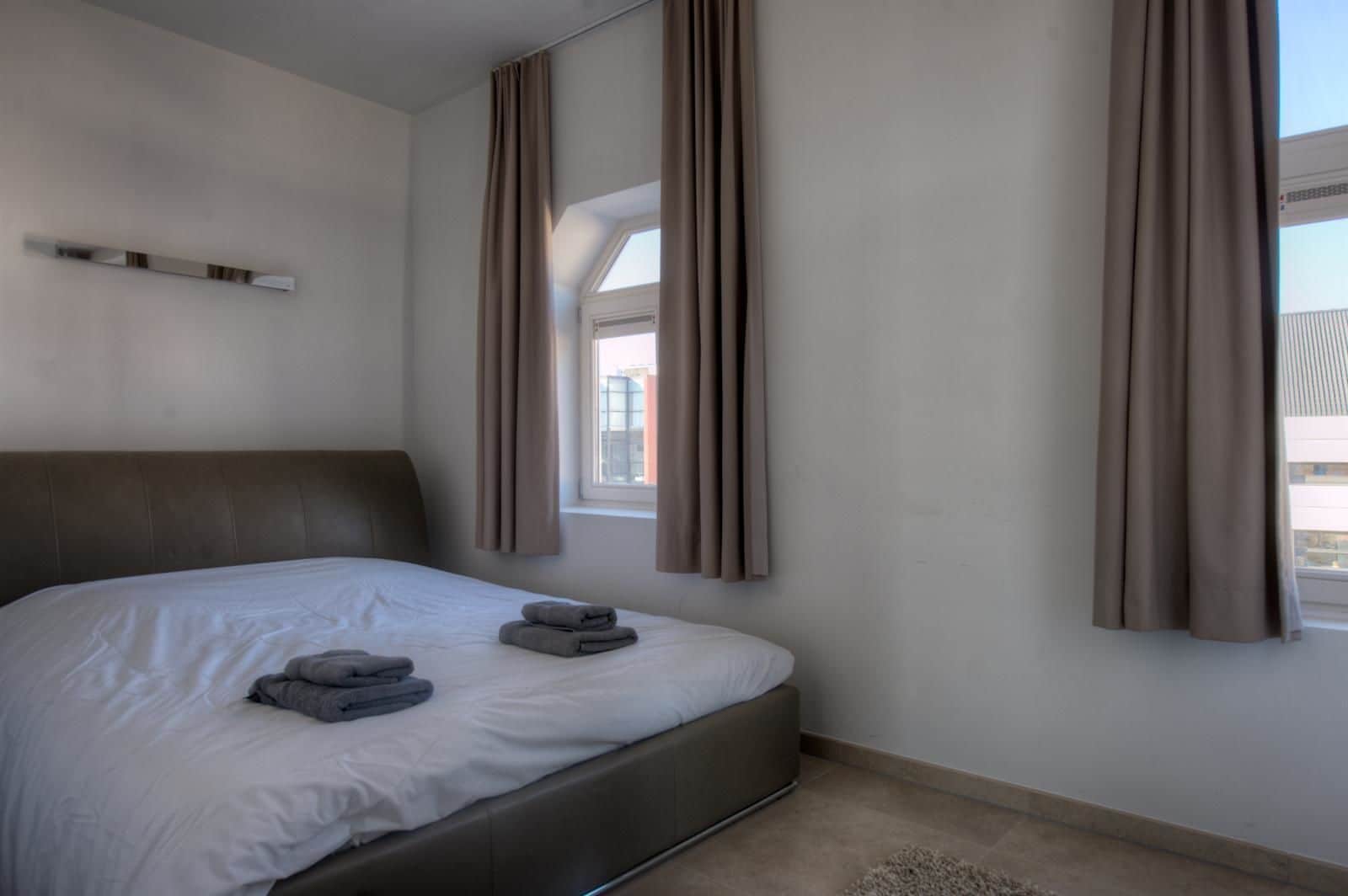 Una habitación de hotel moderna con una cama grande, un cabecero y una ventana con cortinas.