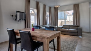 A modern living room with a wooden dining table, black chairs, a grey sofa, and a television mounted on the wall. - Place2stay in Ghent (Ghent)