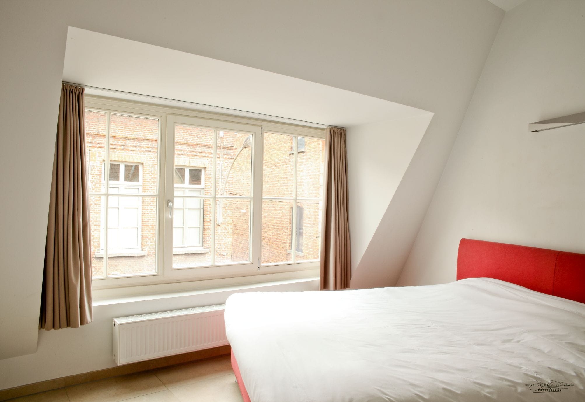 A bedroom with a bed, a window with curtains, and a radiator.