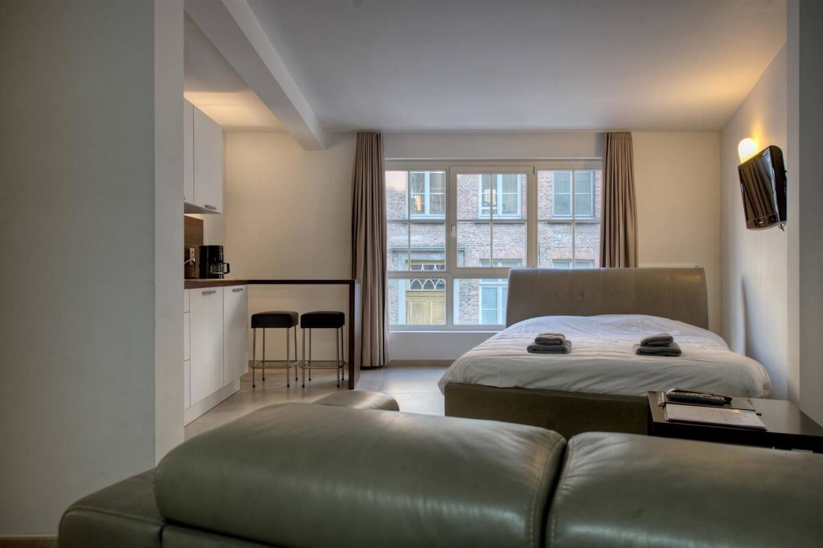 A modern hotel room with a large bed, a small kitchenette, and a view of the city.