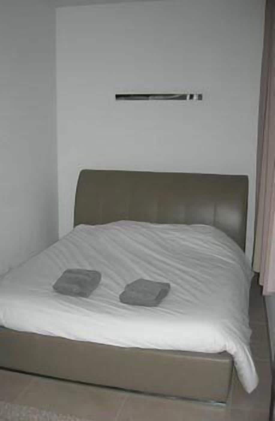 Una cama con cabecera, una almohada y una mesita de noche.