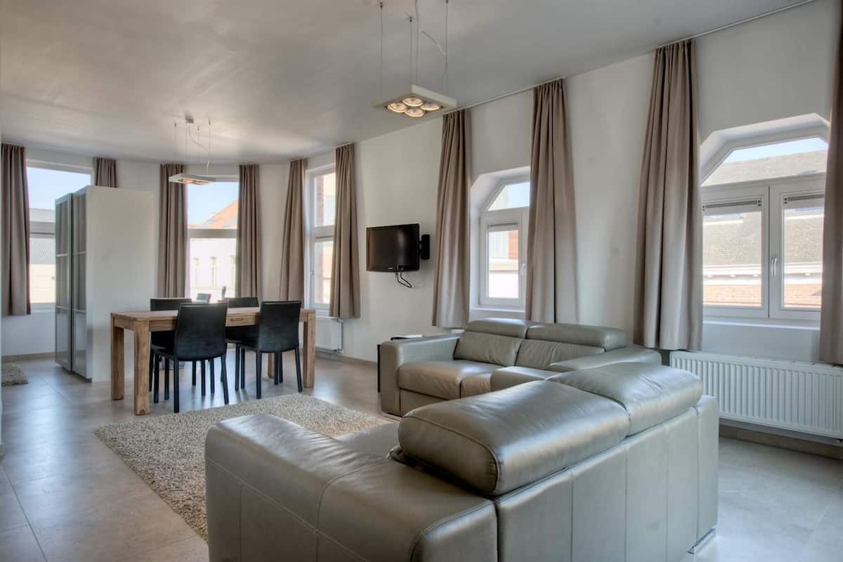 A modern living room with a sofa, dining table, chairs, and a TV.