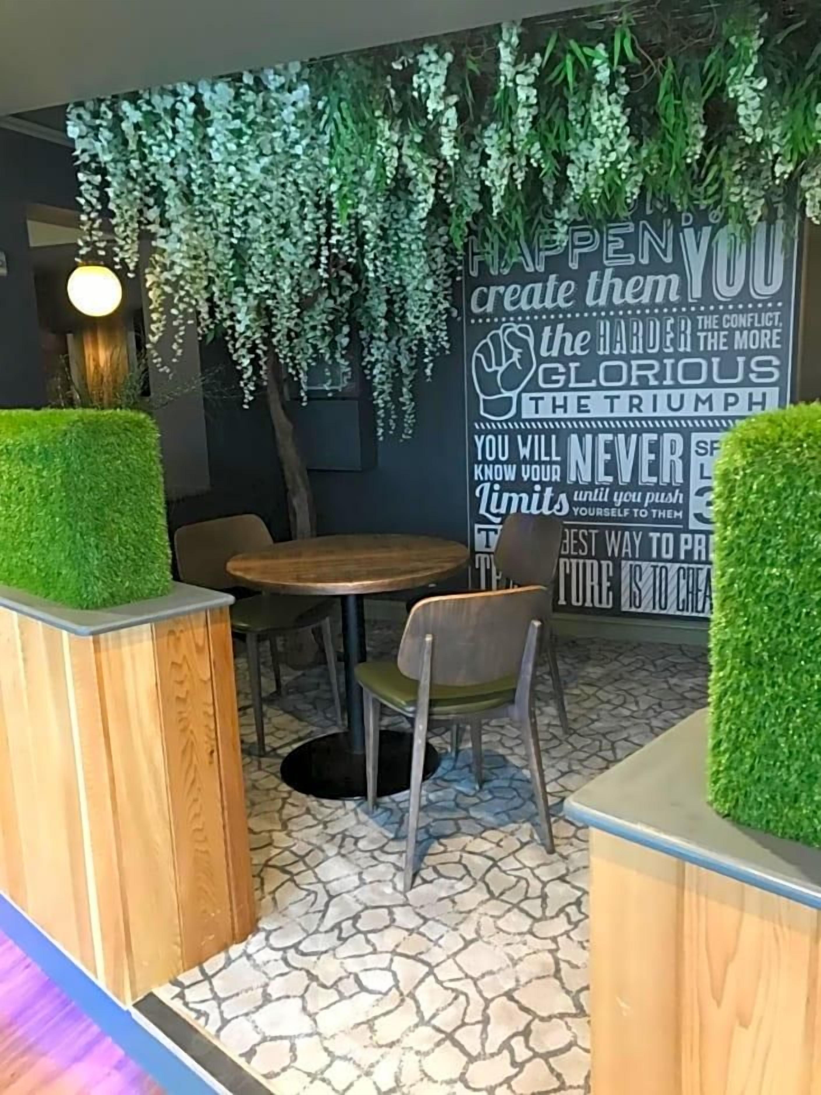 A modern indoor seating area with a round wooden table, chairs, and a decorative wall with motivational quotes.