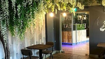 A room with a wooden floor, a table with chairs, a wall with hanging greenery, and a door with a sign.