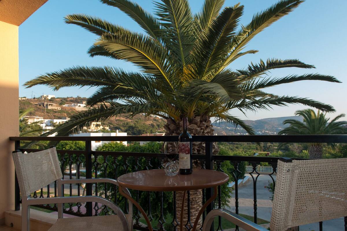 Un balcon avec une table, deux chaises en osier et un palmier en pot.