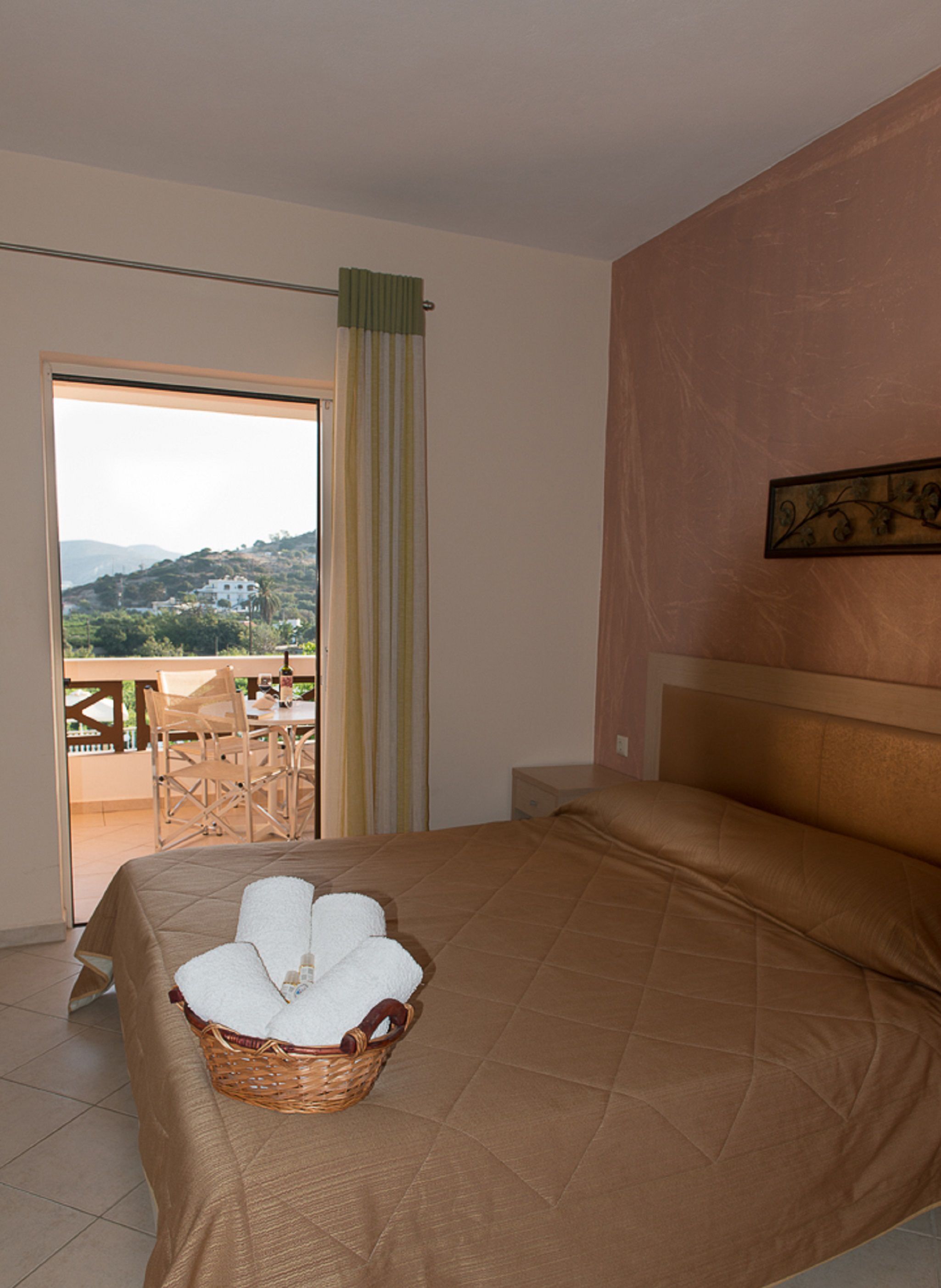 Habitación de hotel con una cama, una cesta de mimbre con toallas, vistas al exterior y un cuadro en la pared.
