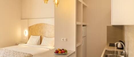 Una camera d'albergo compatta con un letto, comodino, vassoio di frutta e angolo cottura con lavello e fornelli.