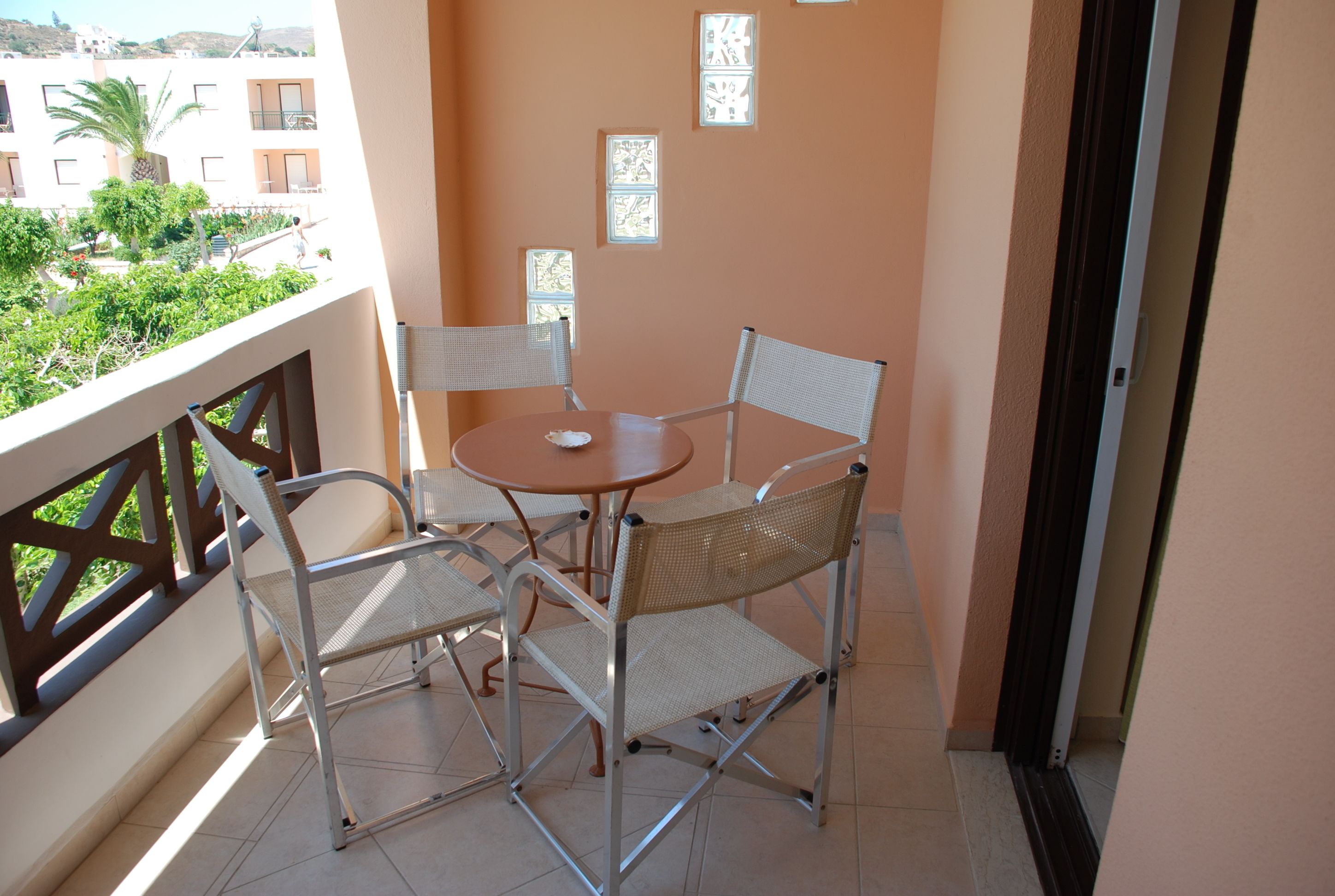 Un balcón con mesa y cuatro sillas, vistas a edificios y vegetación, y decoraciones de pared con diseños.