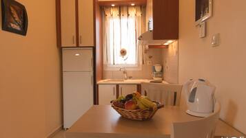 Una cocina compacta con refrigerador, pileta, cafetera y tetera sobre la mesa.