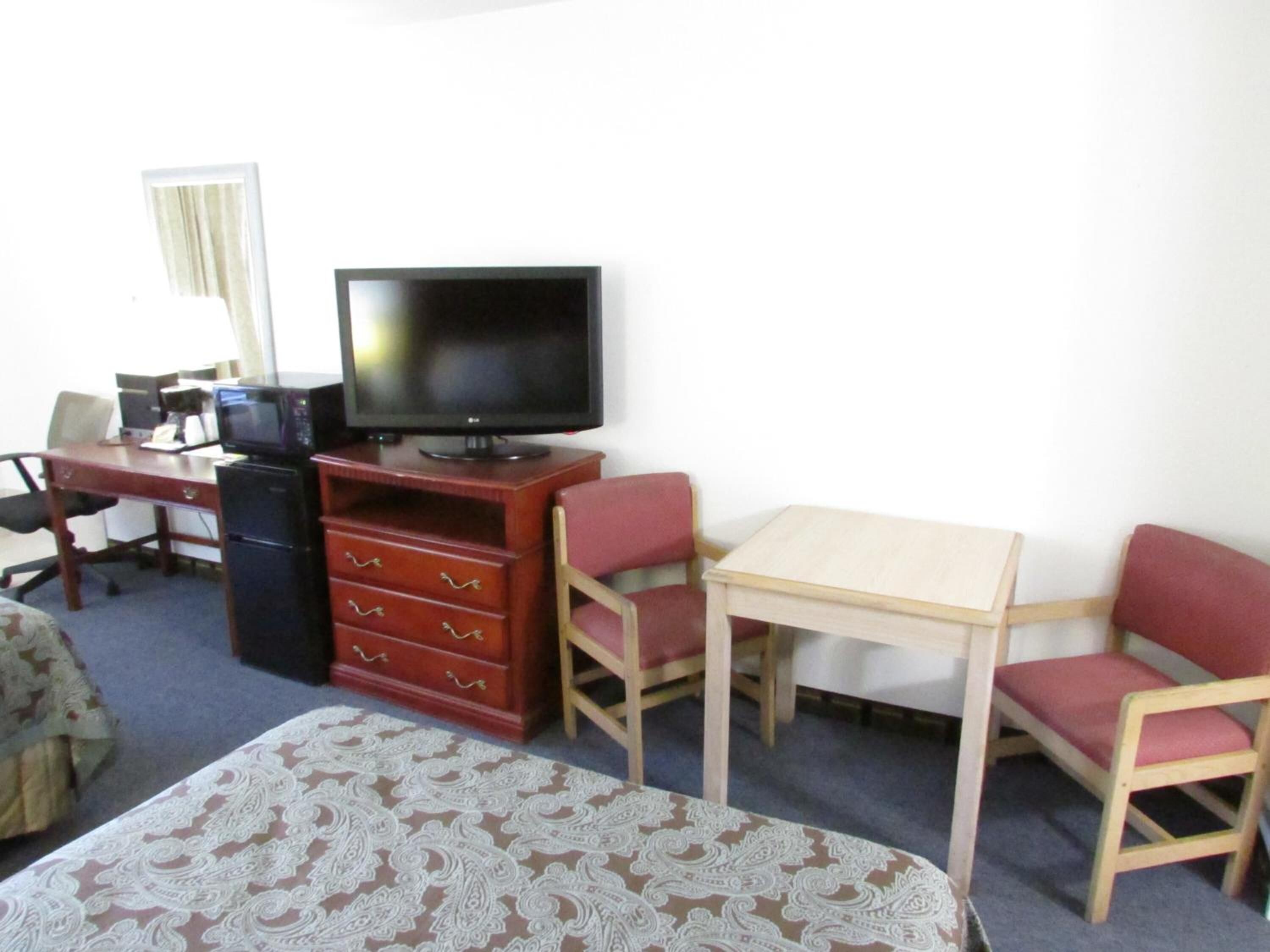 Une chambre d’hôtel comprenant un lit, un bureau avec un ordinateur, une télévision et deux chaises.