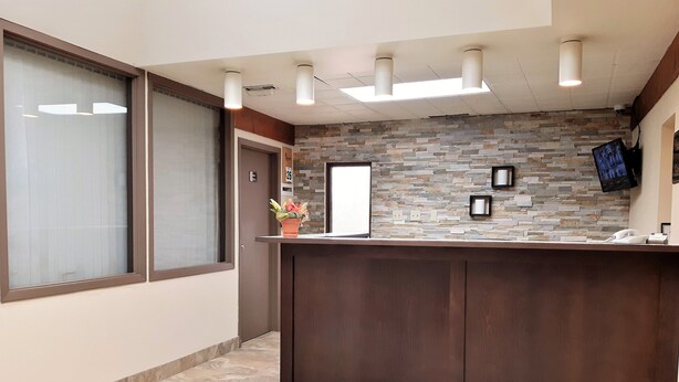 A reception area with a stone wall, a wooden reception desk, a potted plant, and a mounted television. - Lacombe Motor Inn (Lacombe)
