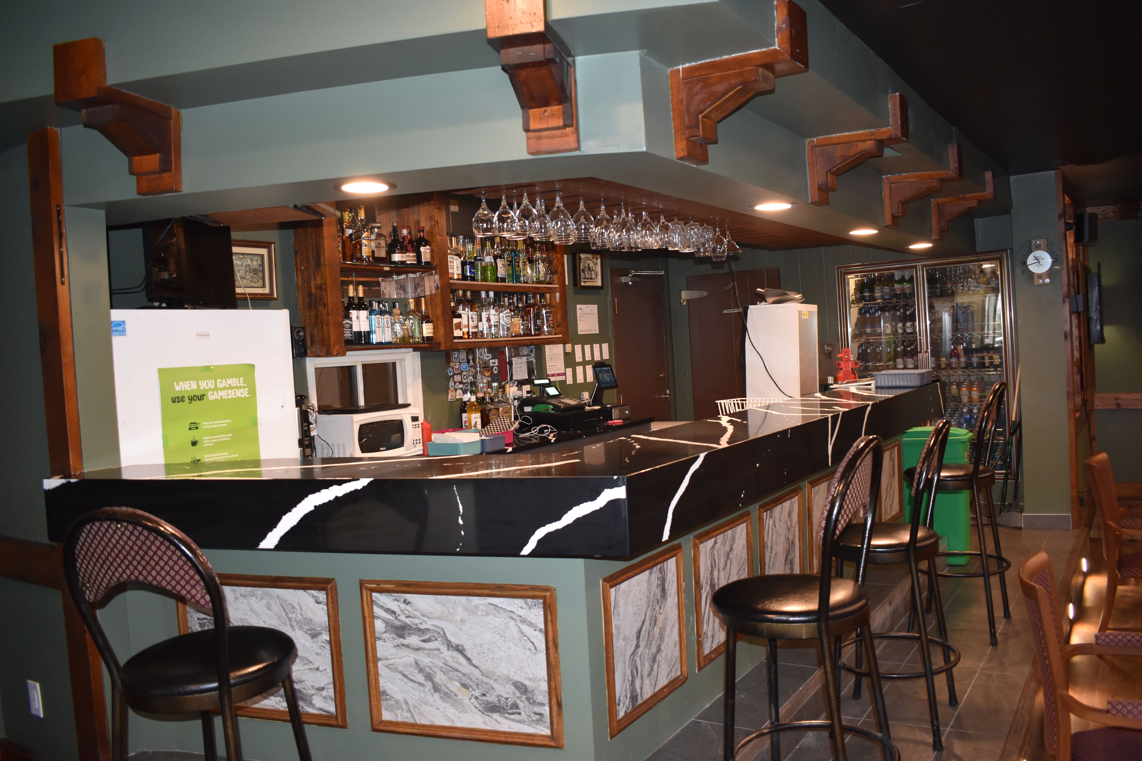 A bar area with a counter, stools, shelves with bottles, and a refrigerator.