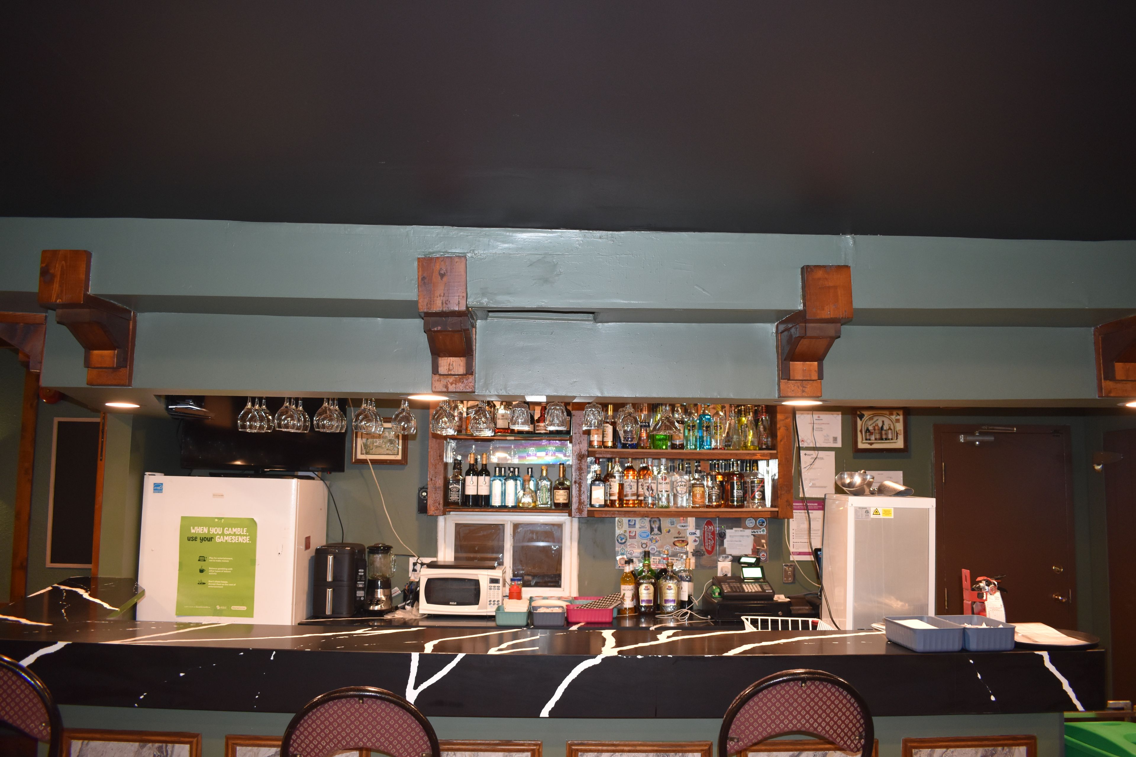 A bar area with a counter, shelves of bottles, a refrigerator, and a sign about gambling.