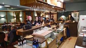 A bar area with stools and tables, bottles of beer, and a variety of glasses on shelves. - Lacombe Motor Inn (Lacombe)