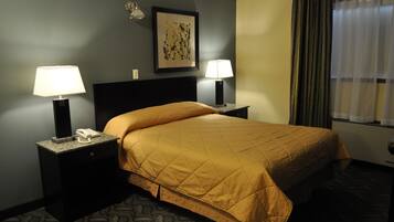 Habitación de hotel con cama, dos mesitas de noche con lámparas, teléfono, un cuadro en la pared y una ventana con cortinas.