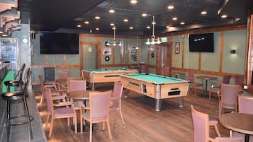 Una sala de billar con mesas de pool, sillas y una zona de bar.