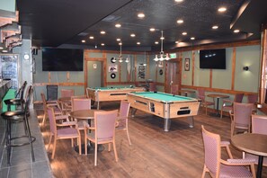 A billiards room with pool tables, chairs, and a bar area. - Lacombe Motor Inn (Lacombe)