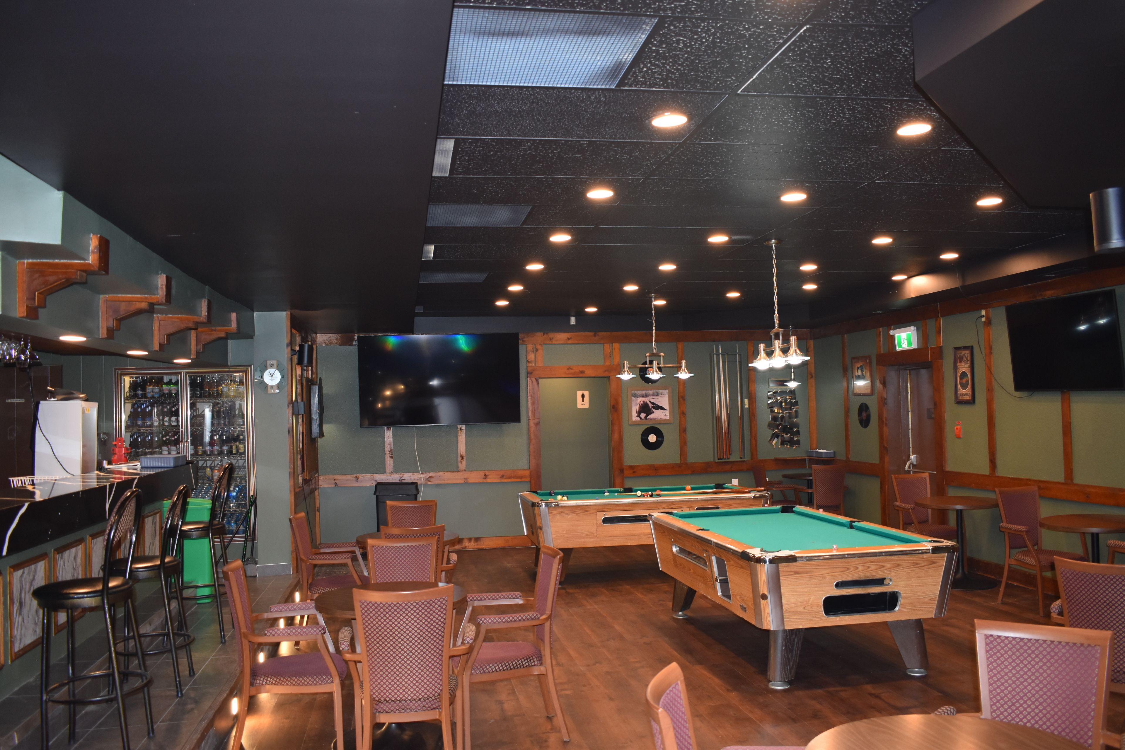 A bar area with pool tables, chairs, and a bar counter with a clock and bottles.