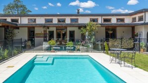 Una casa moderna con piscina, un patio cubierto y un jardín cercado.