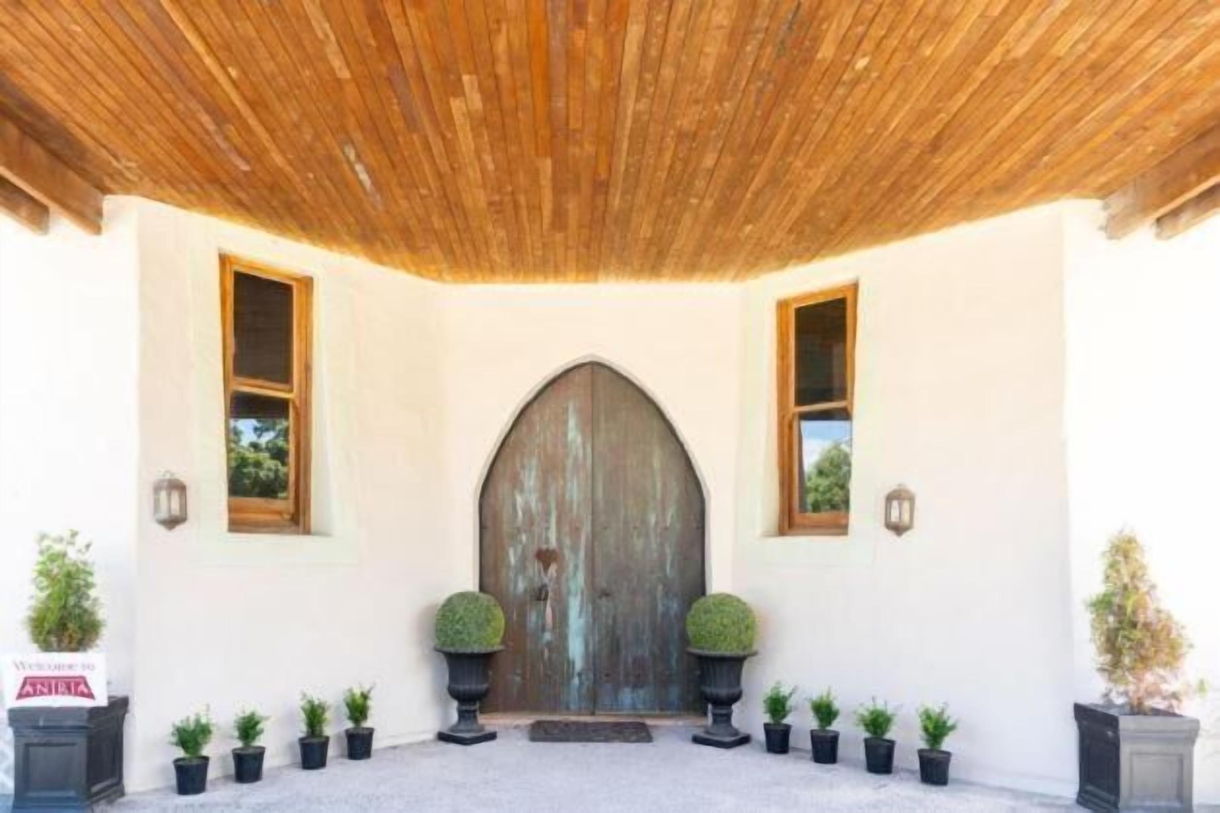 A building entrance with a wooden door, potted plants, and a tiled floor.