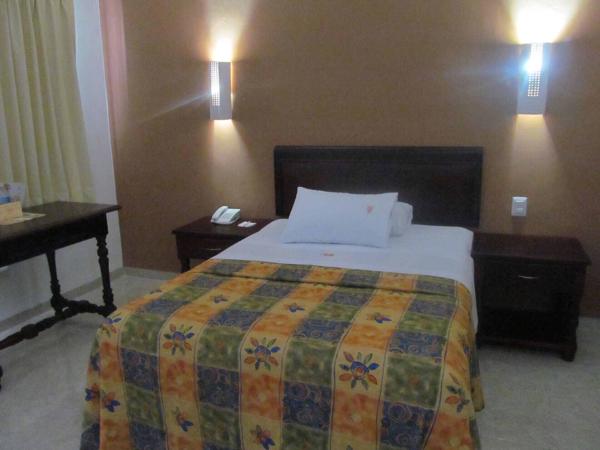 Une chambre d’hôtel avec un lit bien fait, une table de chevet avec un téléphone et deux lampes fixées au mur.