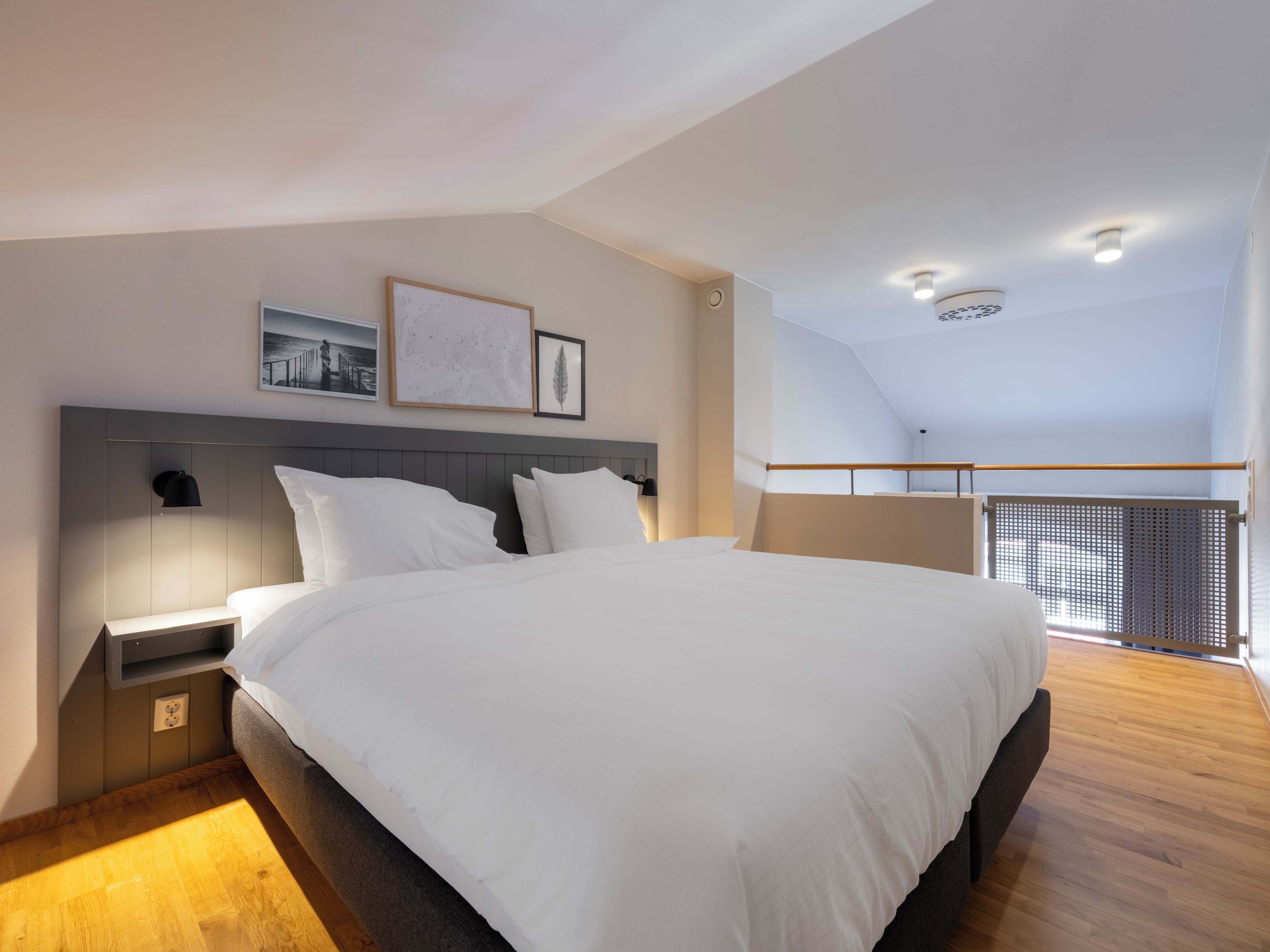 Un dormitorio moderno con una cama grande, una mesita de noche, una lámpara de pared y un cuadro enmarcado.