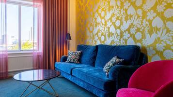 A room with a blue sofa, a round table, a red chair, and a yellow floral wallpaper.