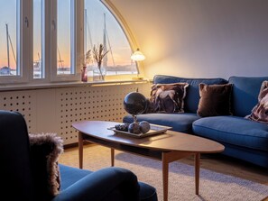 A modern living room with a blue sofa, a wooden coffee table, and a view of the harbor with cranes. - Mercure Gothenburg (Vastra Frolunda)