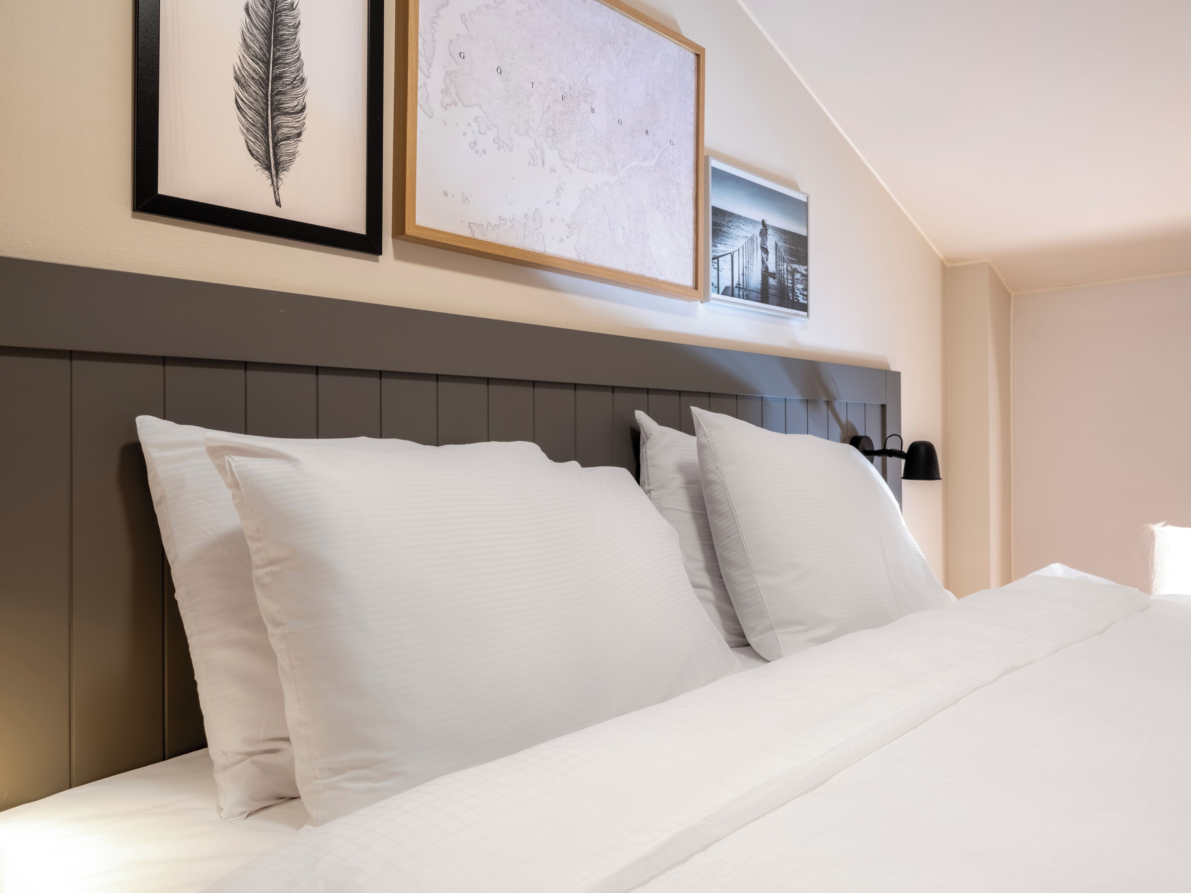 A neatly made bed with white linens and pillows, a headboard with vertical panels, and framed artwork on the wall above.