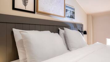 A neatly made bed with white linens and pillows, a headboard with vertical panels, and framed artwork on the wall above.