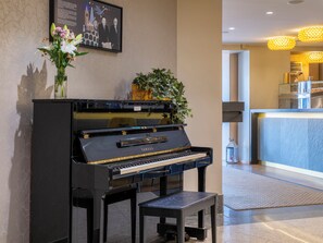A Yamaha grand piano in a lobby area with a framed picture above it, a potted plant, and a small table in front. - Mercure Gothenburg (Vastra Frolunda)