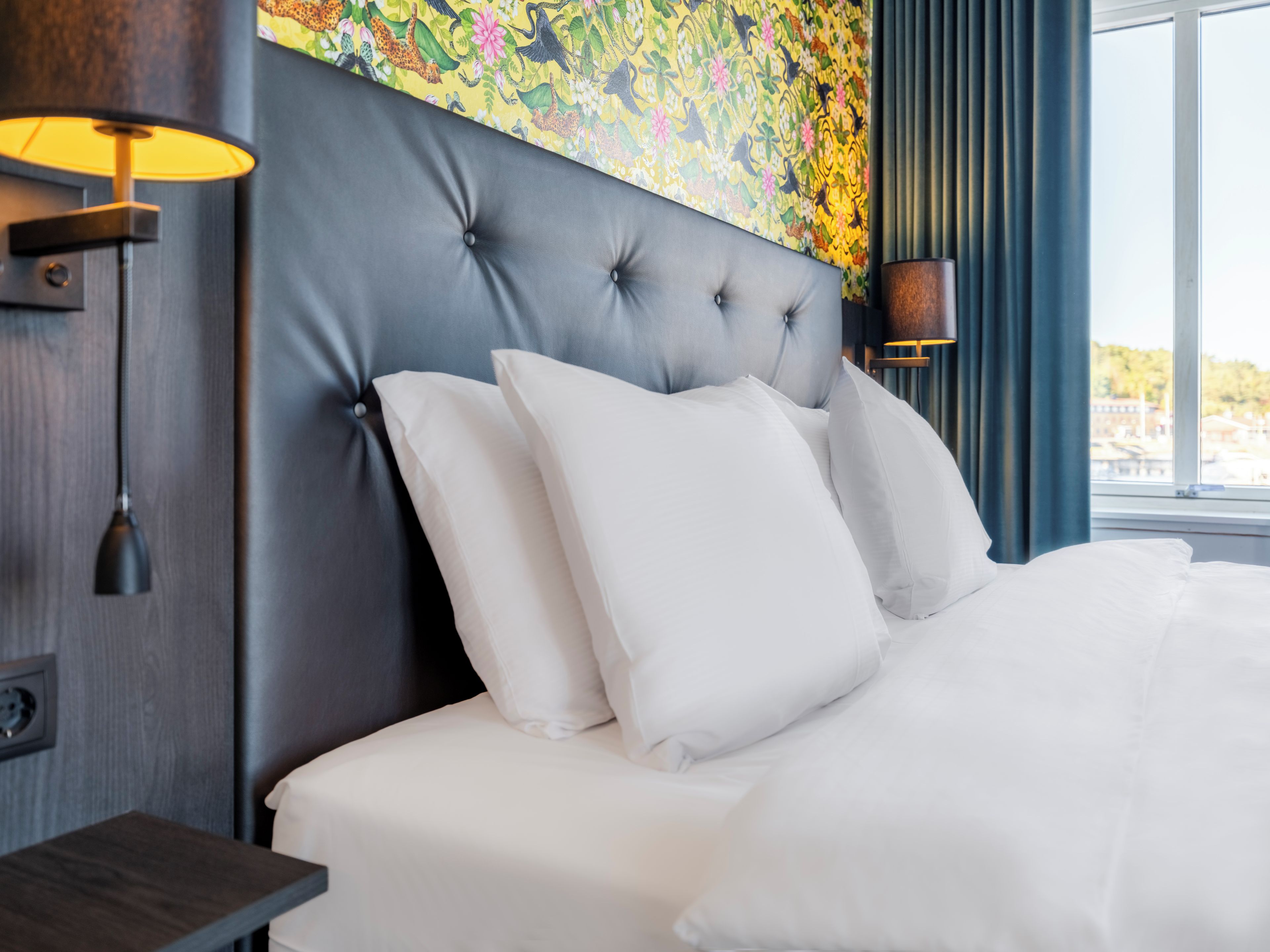 Une chambre d’hôtel avec une tête de lit capitonnée, du linge de lit blanc et une fresque murale florale aux couleurs vives.