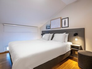 A modern bedroom with a large bed, a bedside table, a nightstand, a lamp, and a small round ottoman. - Mercure Gothenburg (Vastra Frolunda)