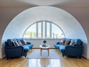 A room with a semi-circular ceiling, two blue sofas, a round wooden table, and a large window with a view of greenery. - Mercure Gothenburg (Vastra Frolunda)