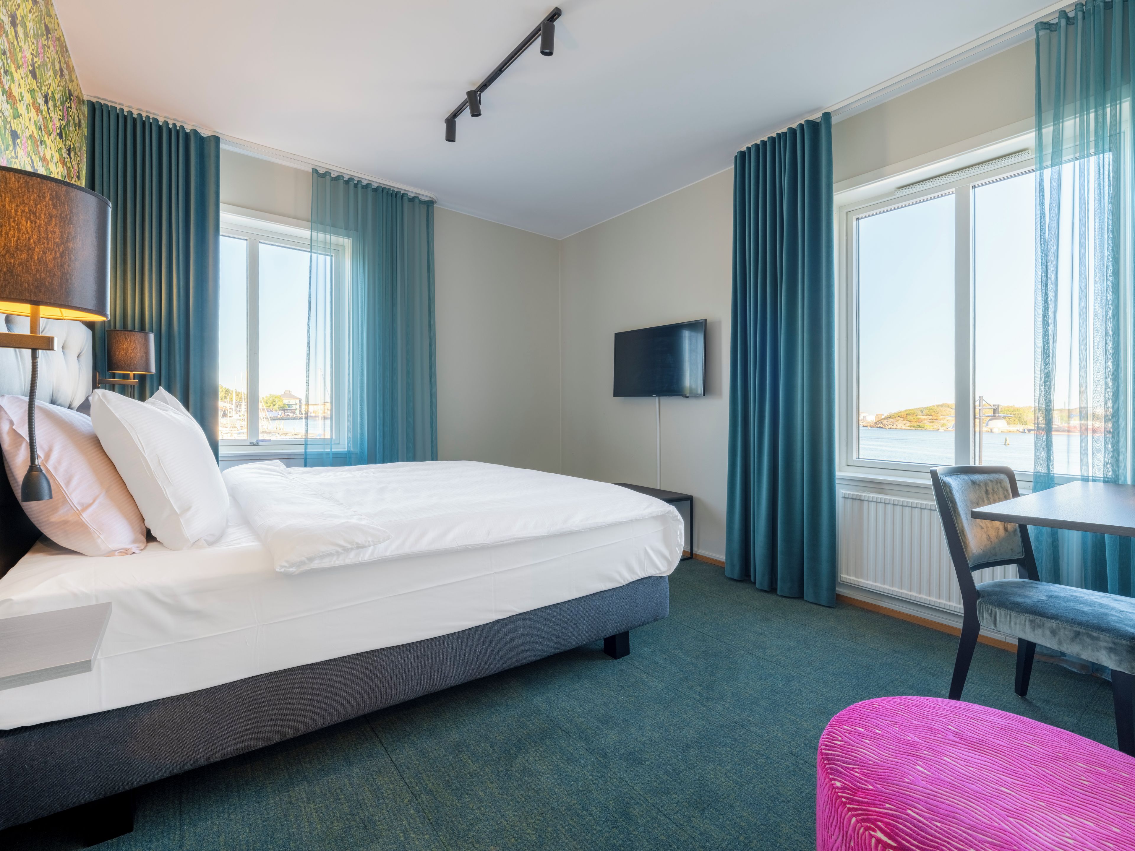 A hotel room with a bed, a desk, a chair, a TV, and a window with curtains.