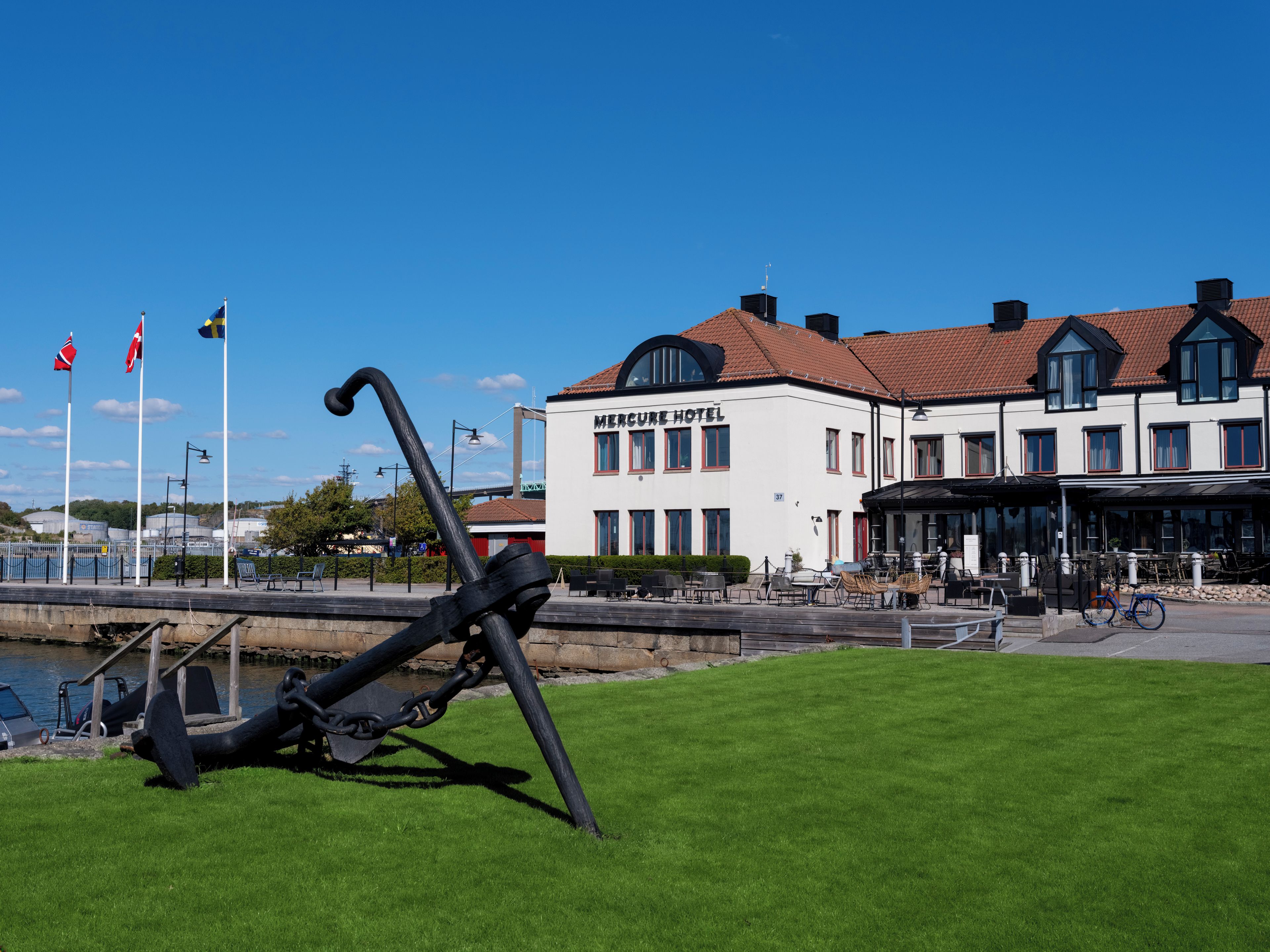A waterfront hotel with a white facade, a dock area with boats, and a grassy foreground.