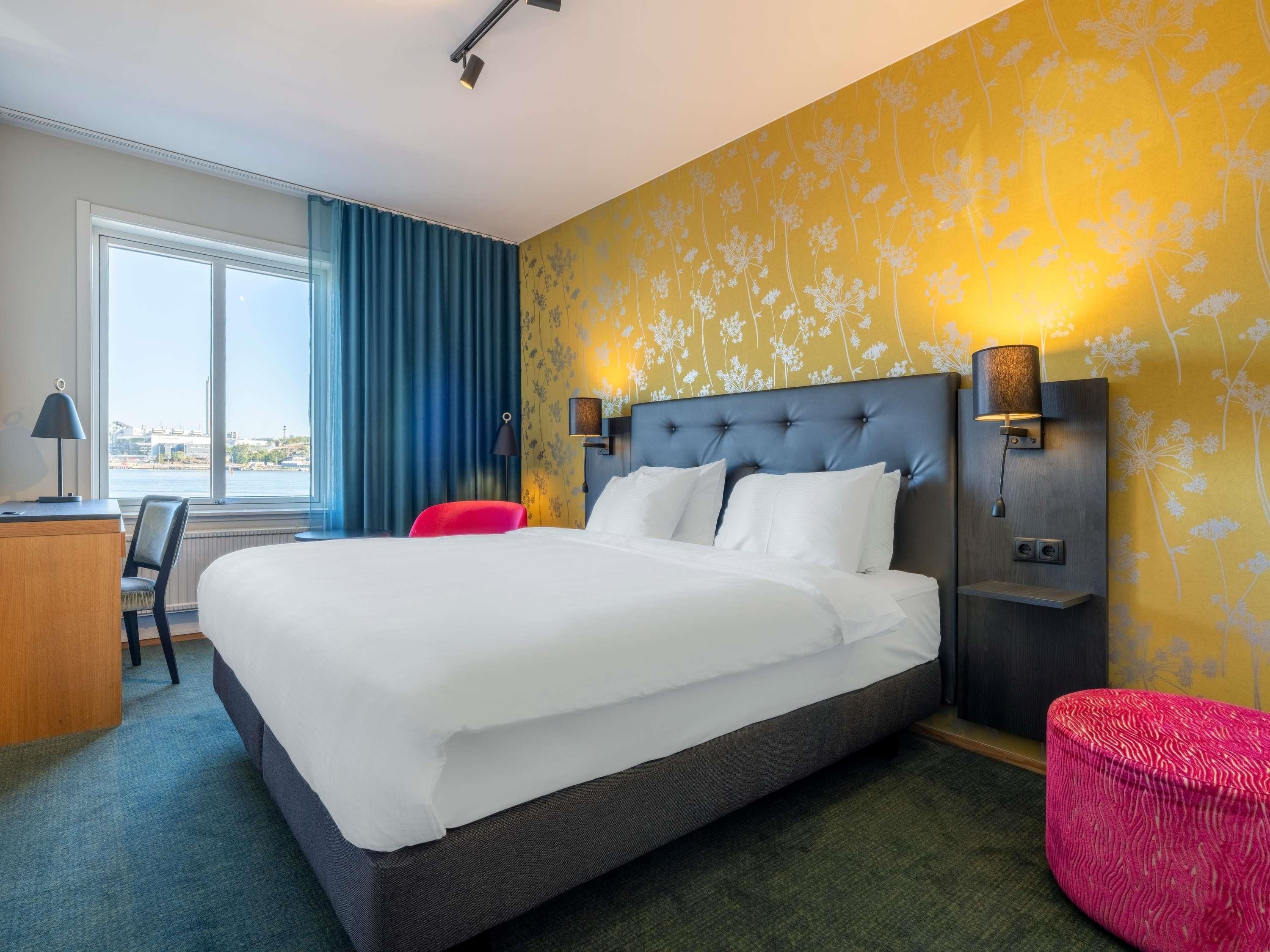 Ein Hotelzimmer mit einem großen Bett, einem Schreibtisch, einem Sessel und Blick ins Freie.