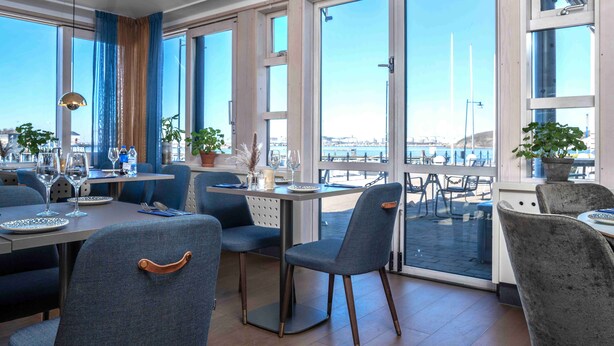A restaurant with large windows, tables, chairs, and potted plants. - Mercure Gothenburg (Vastra Frolunda)