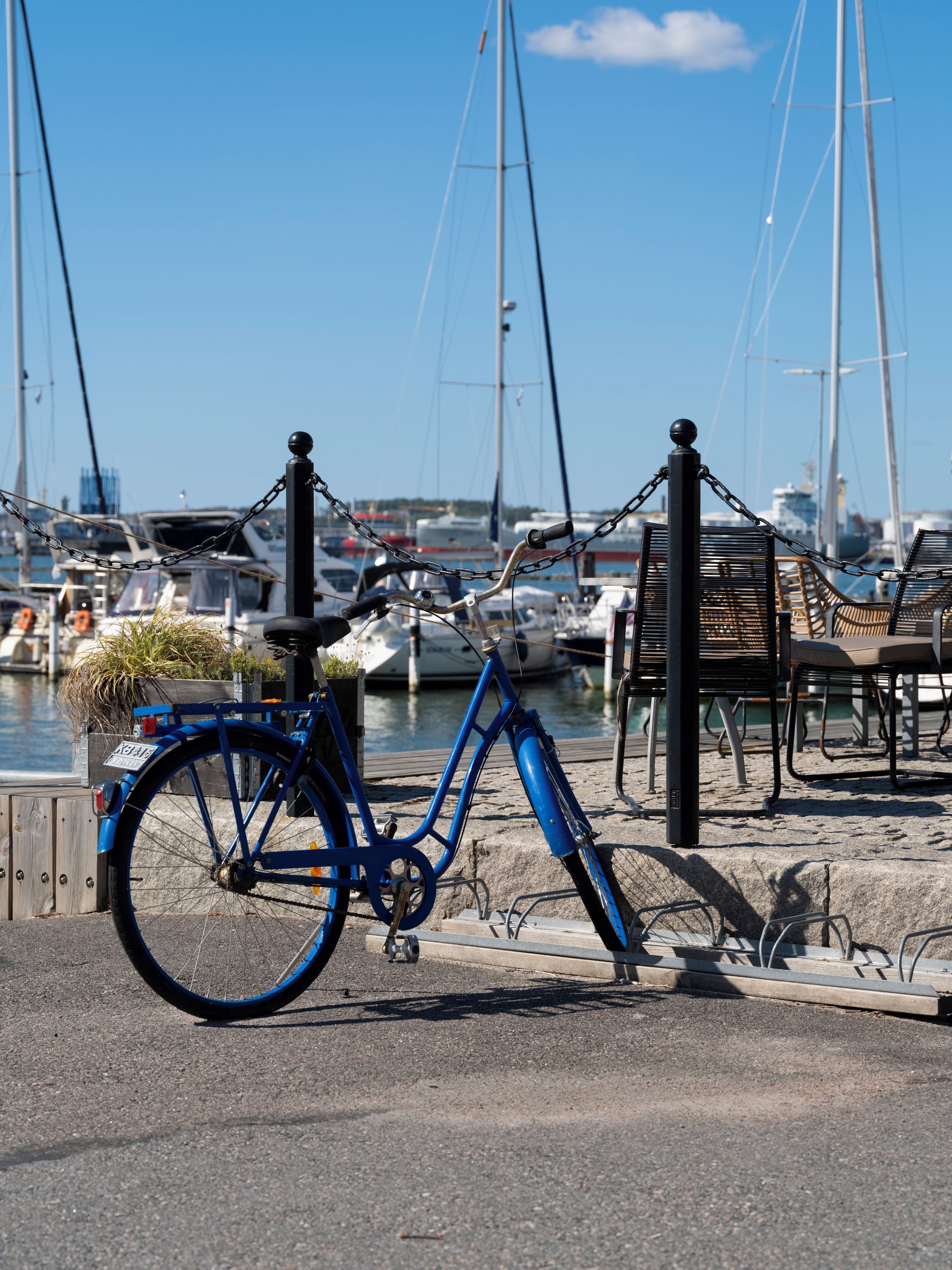 A blue bicycle parked at a dock with boats in the background.