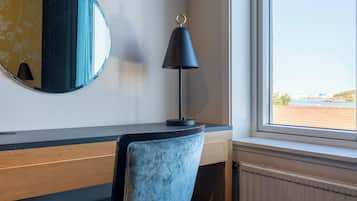 A room with a desk, a chair, a lamp, a round mirror, and a window with a view.