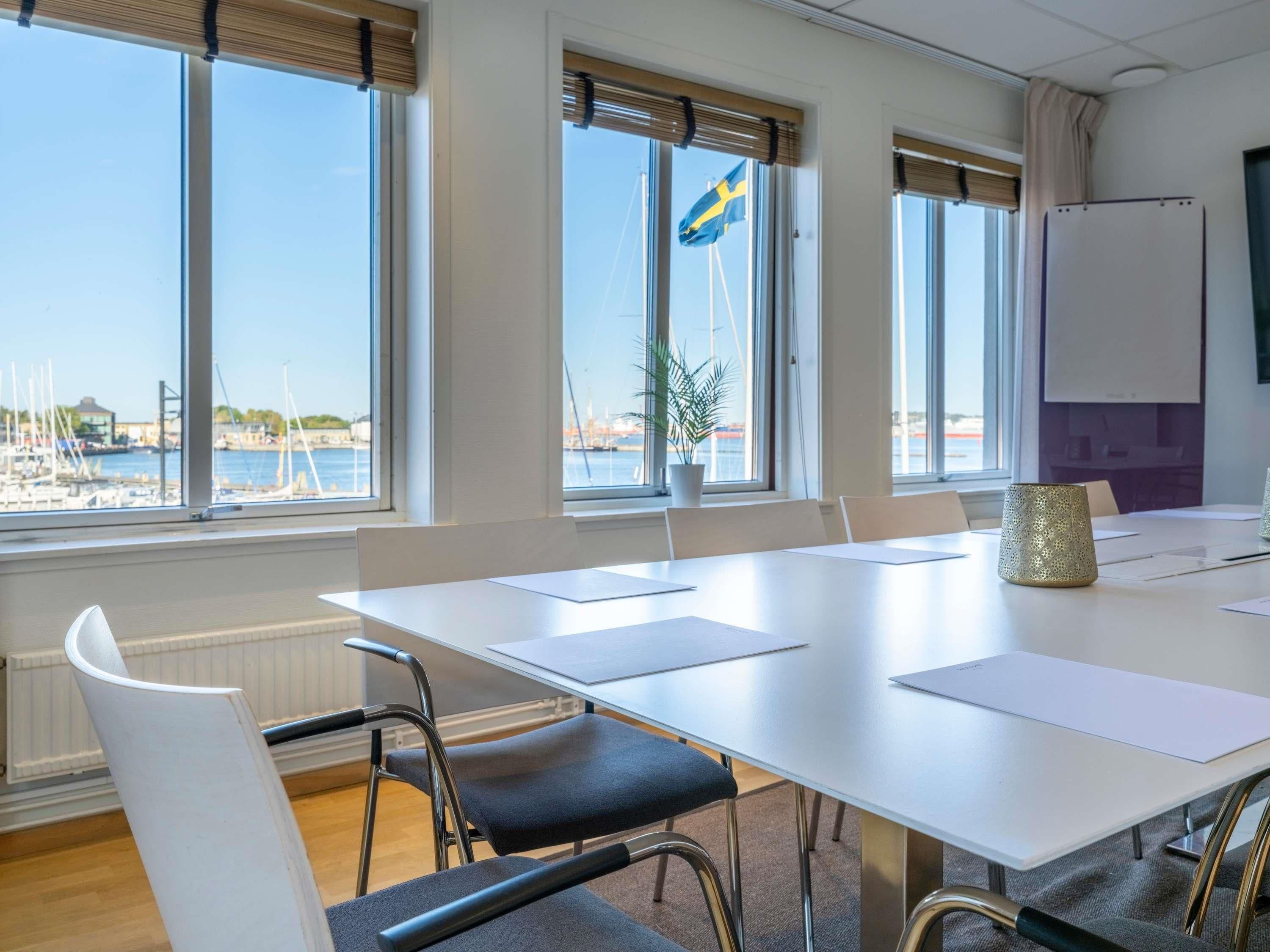 A conference room with a view of a marina, white tables, chairs, and a whiteboard.