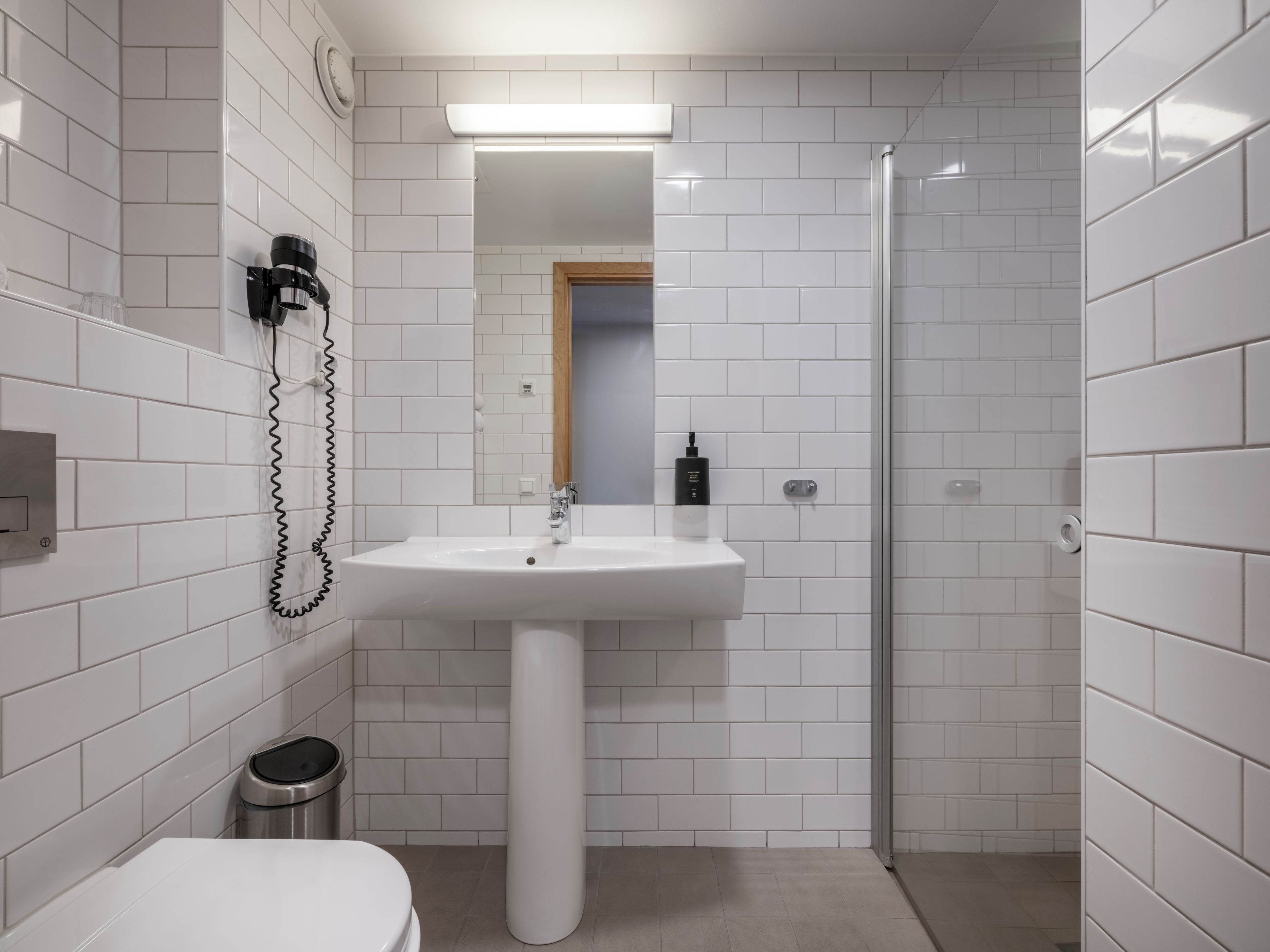 Een moderne badkamer met witte metrotegels, een wastafel op voet, een glazen douchecabine en een toilet.