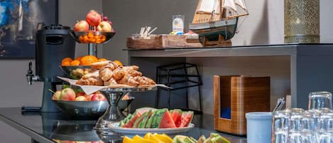 A buffet table with various food items including fruits, pastries, and a ship model.