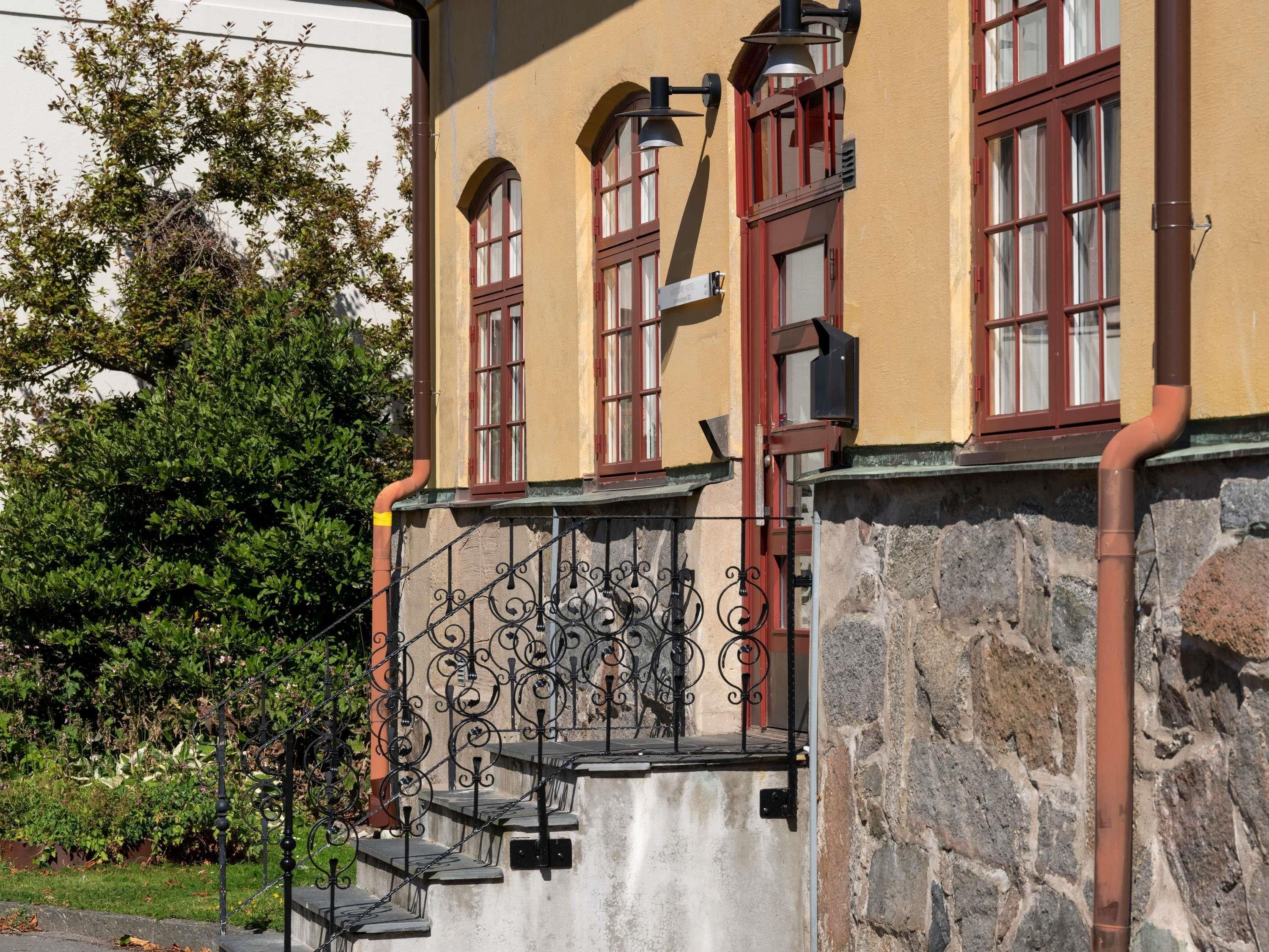 A building with a stone facade, red-framed windows, and a wrought iron gate.