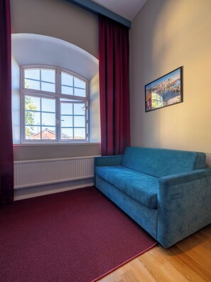 A room with a blue sofa, a red curtain, a window with a view of buildings, and a framed picture on the wall. - Mercure Gothenburg (Vastra Frolunda)