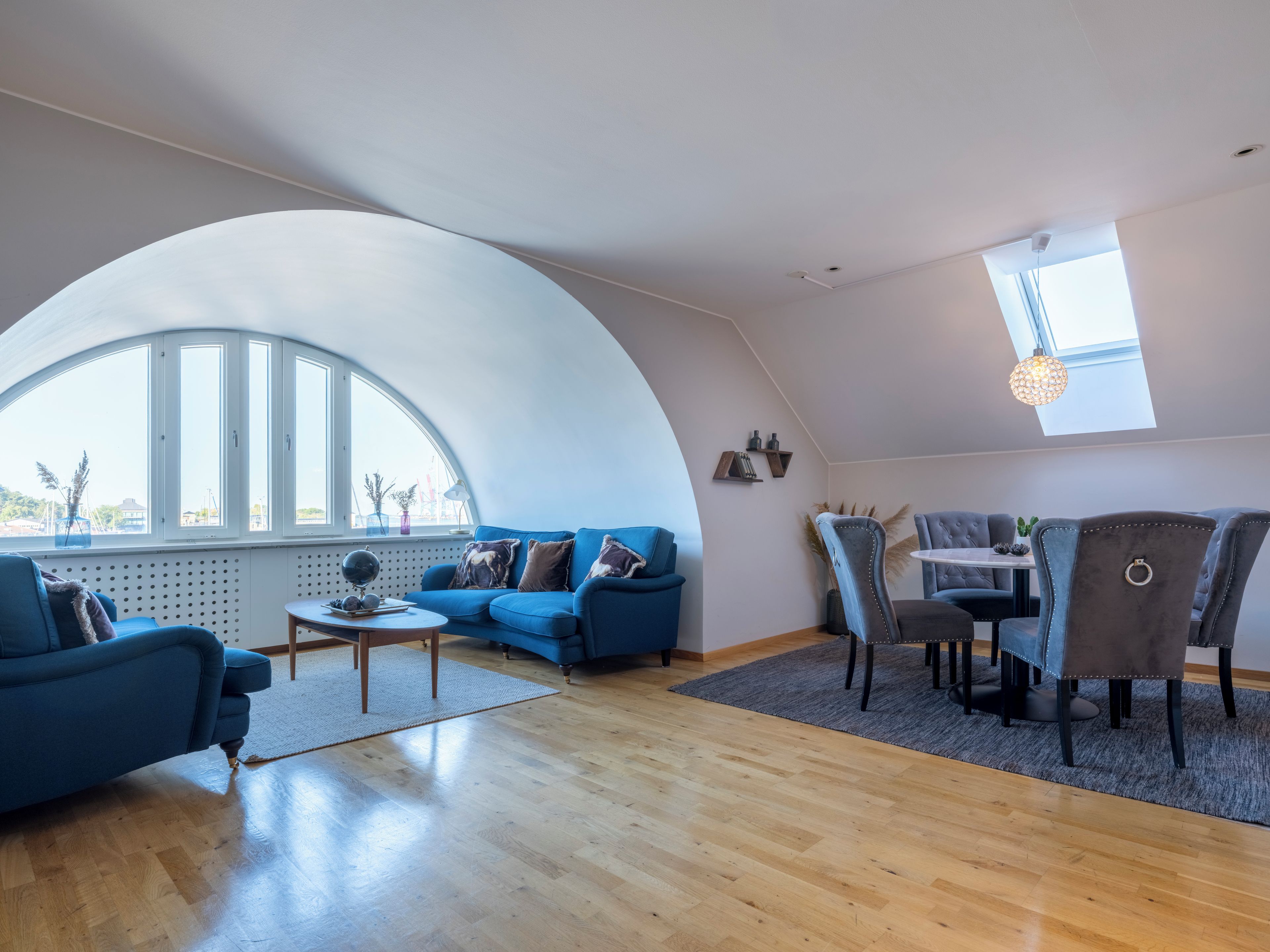 A spacious living area with a curved ceiling, a blue sofa, a dining table, and chairs.