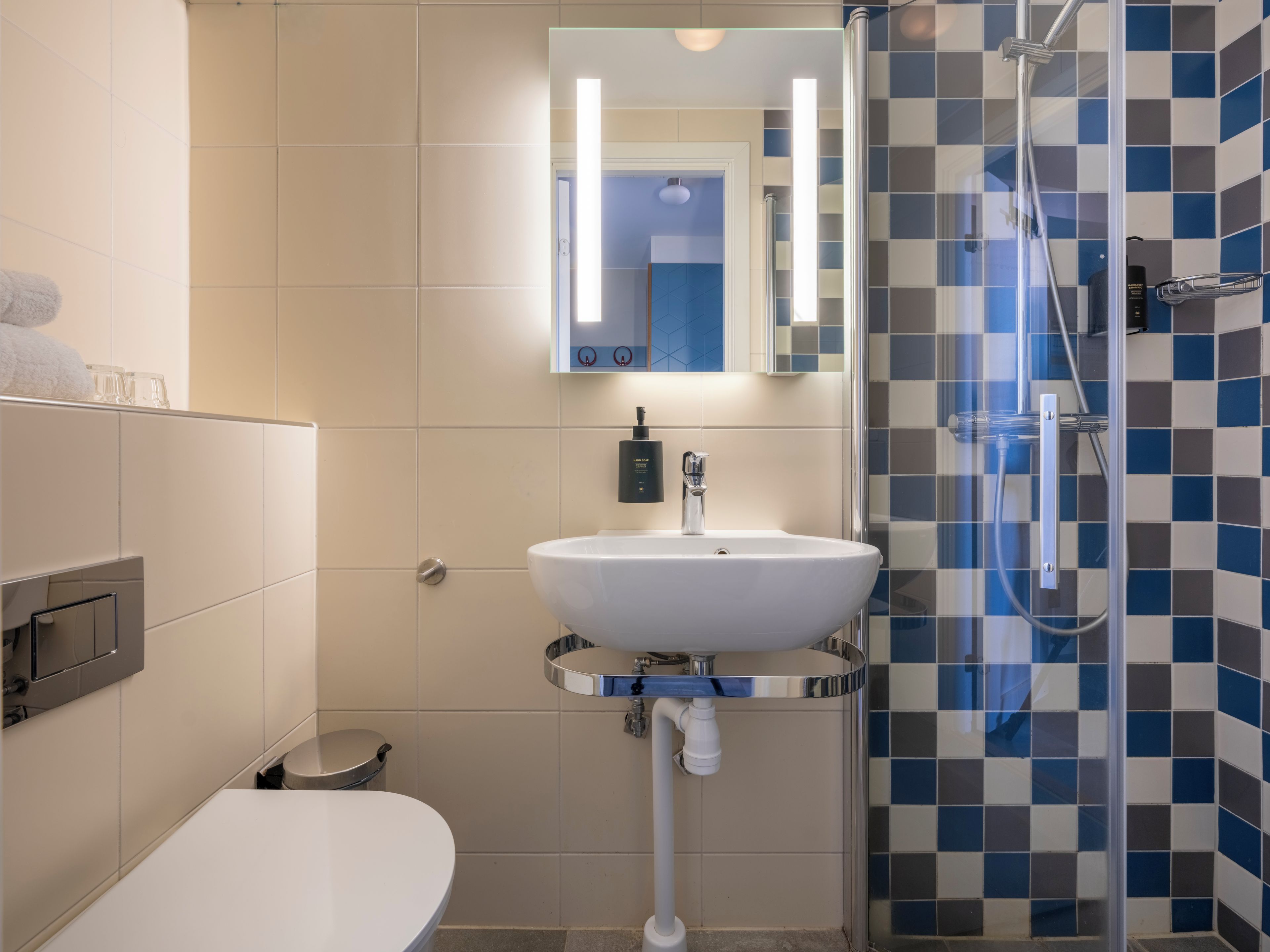 Un baño con un lavamanos blanco, un espejo, cabina de ducha y un inodoro.