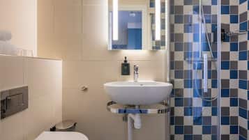 Un baño con un lavamanos blanco, un espejo, cabina de ducha y un inodoro.