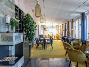 A modern dining area with a large plant, a fireplace, and a yellow patterned carpet. - Mercure Gothenburg (Vastra Frolunda)